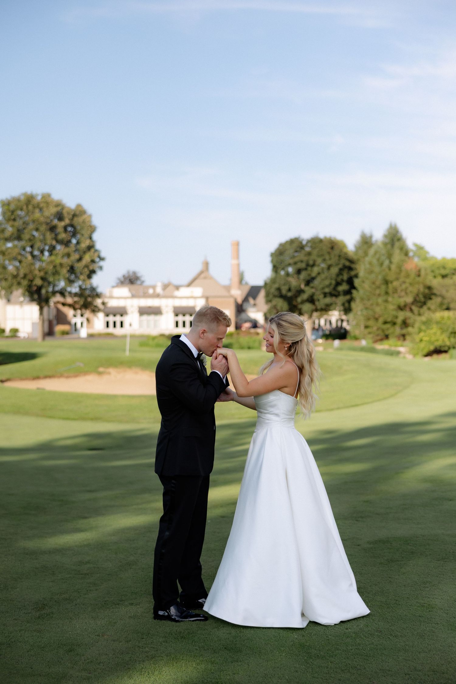 Bride and groom share a tender dance on a golf course with a grand estate building in the background.