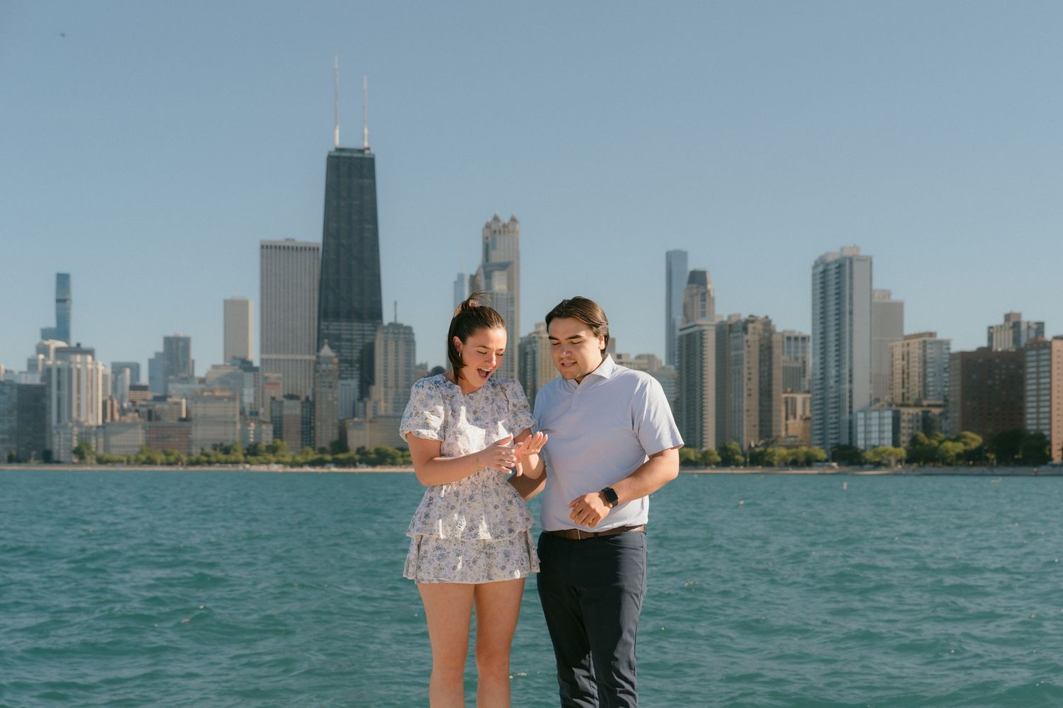 Happy engaged couple admiring ring by Lake Michigan with Chicago skyline.