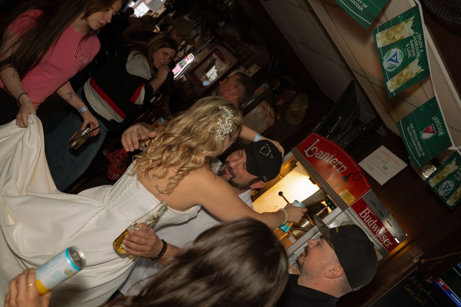 Bride in white dress dancing and kissing at a crowded wedding reception bar celebration.