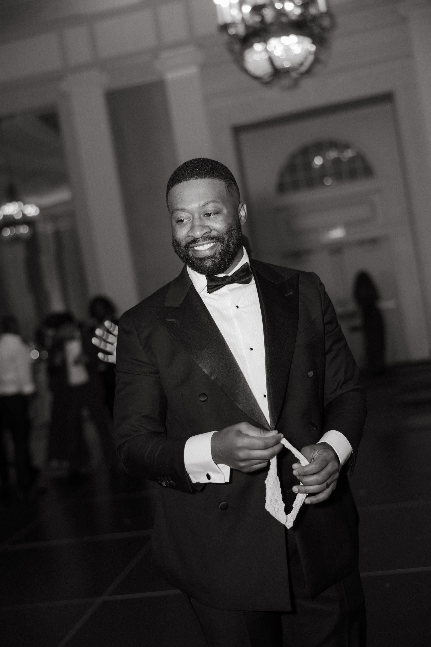 Smiling man in elegant black tuxedo with bow tie poses at formal event in black and white photo.