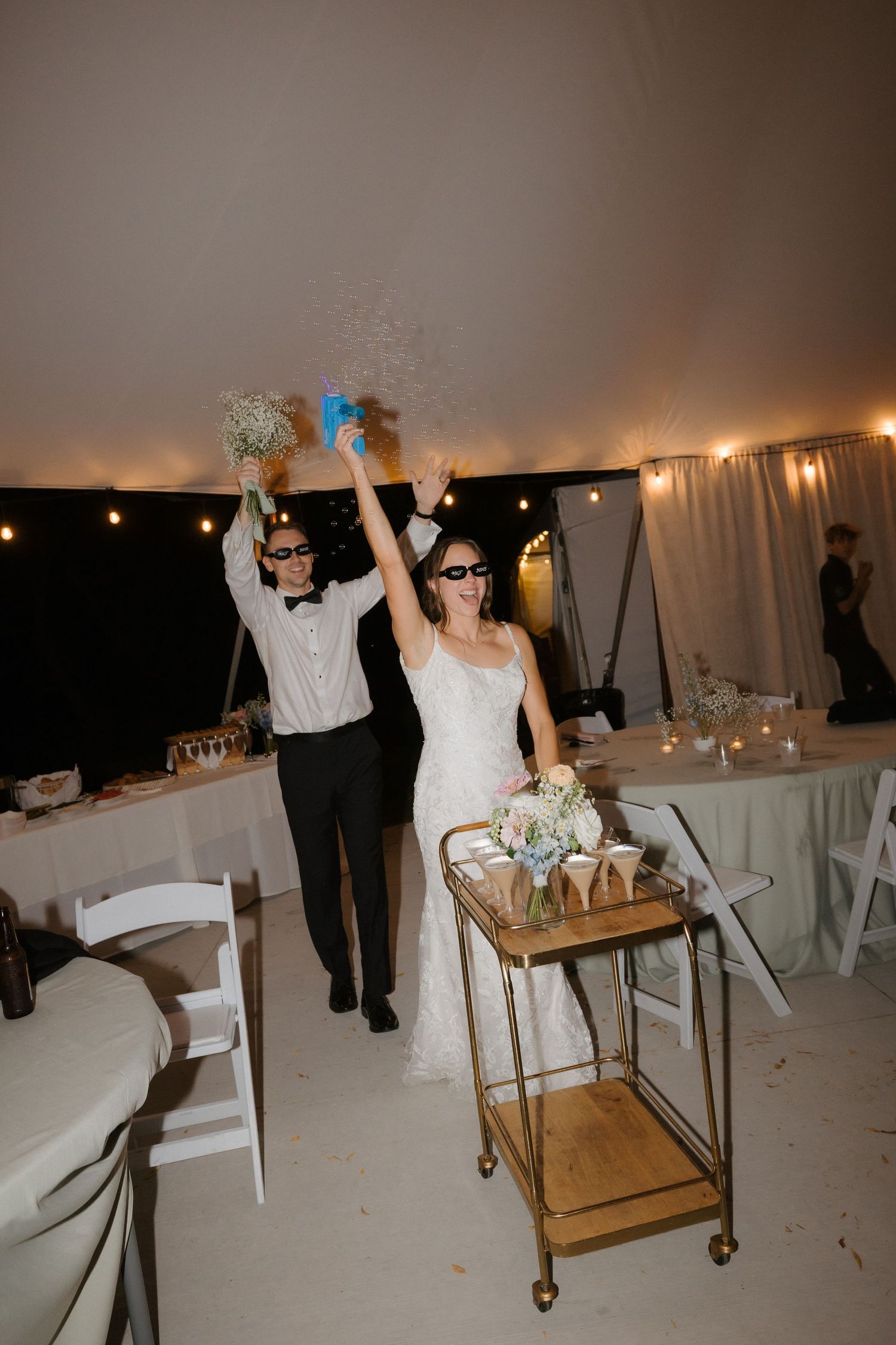 Bride and groom in sunglasses make a grand entrance into their wedding reception tent with confetti.