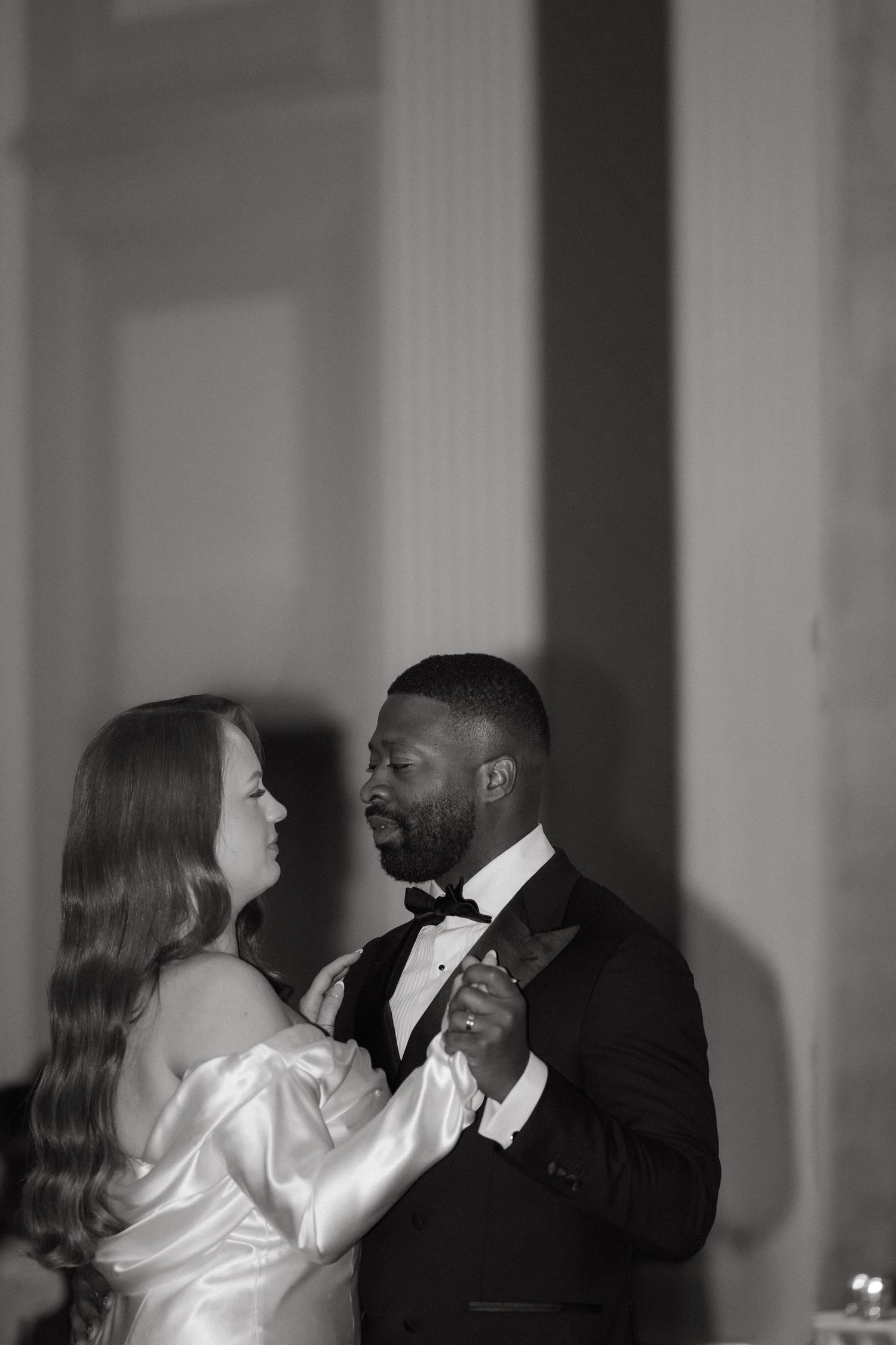 Black and white photo of an interracial couple sharing a first dance at their elegant wedding reception.