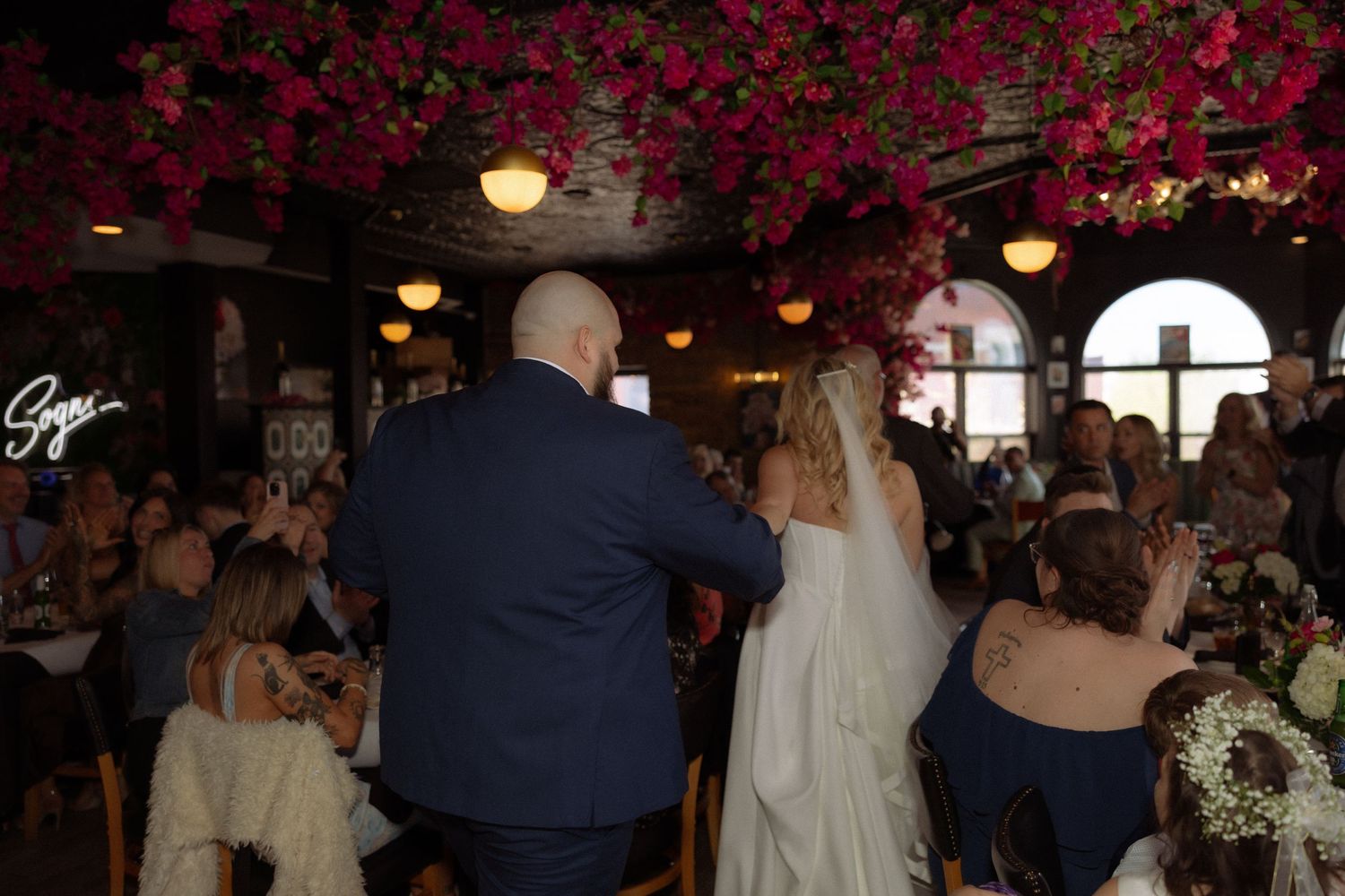 Bride and groom enter wedding reception under stunning floral ceiling of pink flowers in elegant venue.