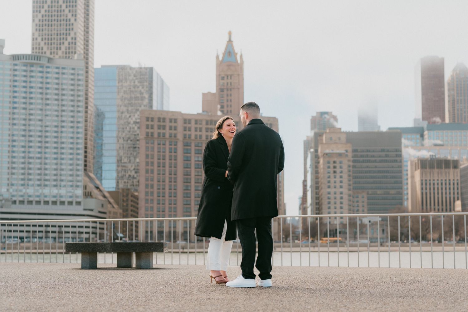Couple sharing a tender moment on Chicago waterfront plaza with misty urban skyline in background.