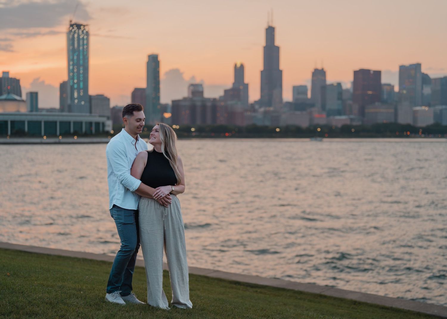 Couple cuddling on a grassy lakefront with the stunning Chicago skyline at sunset.