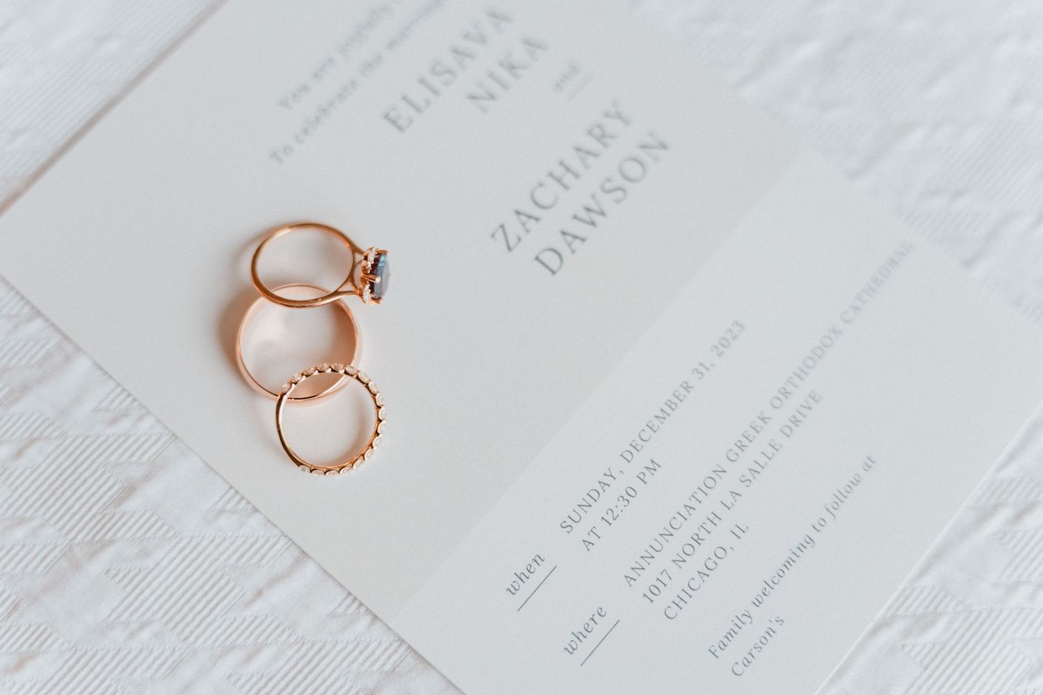 Two gold wedding rings rest on an elegant white wedding invitation for Zachary Dawson.
