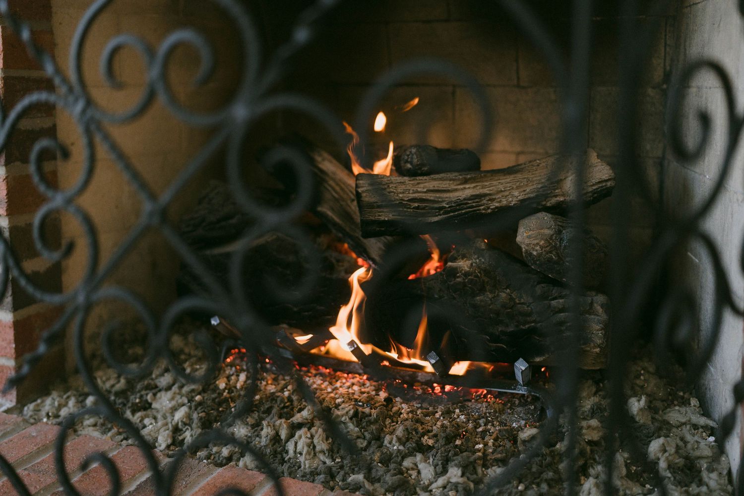 Warm fire burning in ornate black wrought iron fireplace with glowing embers and logs.