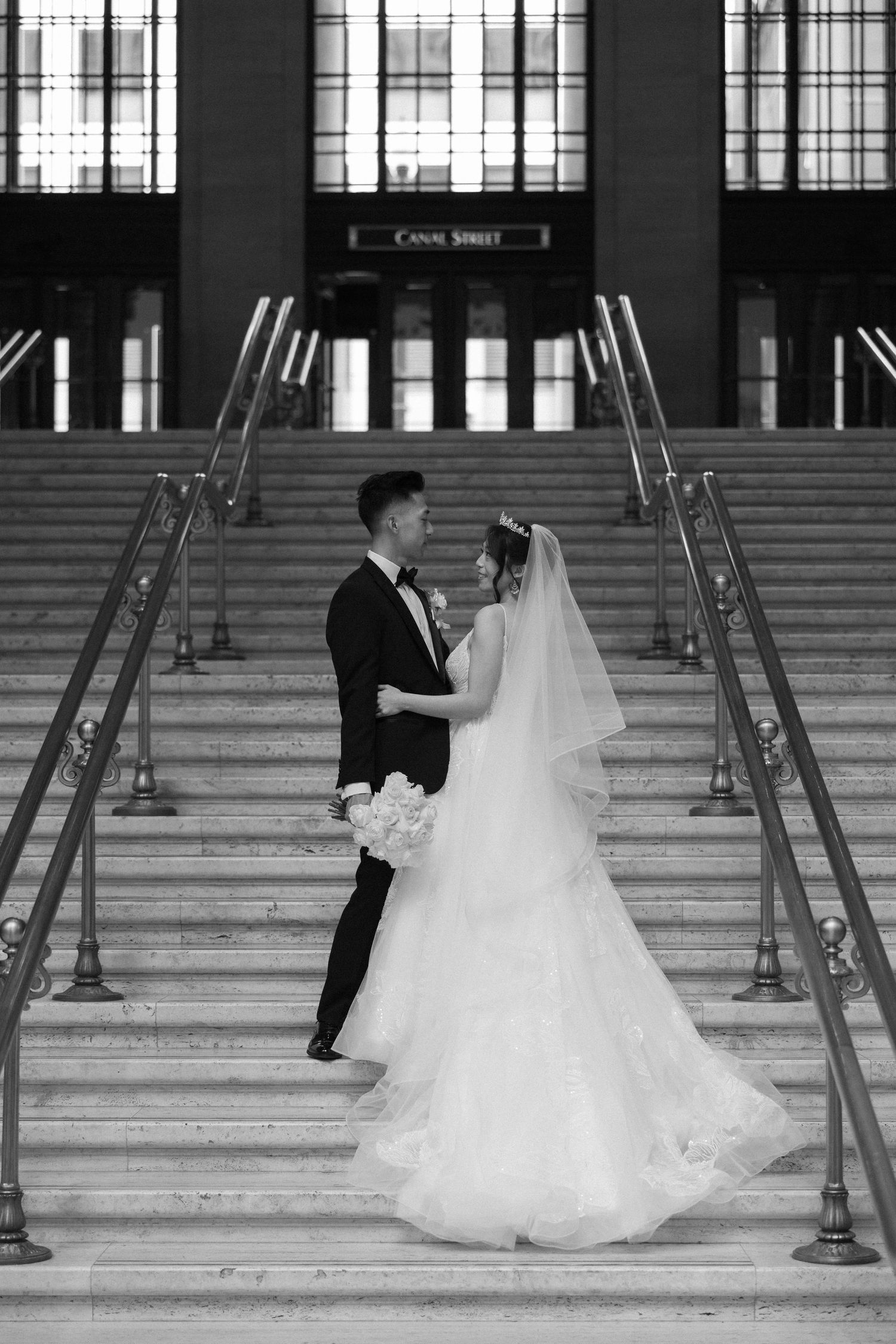 Bride and groom share romantic embrace on grand staircase steps at Canal Street station in black and white.