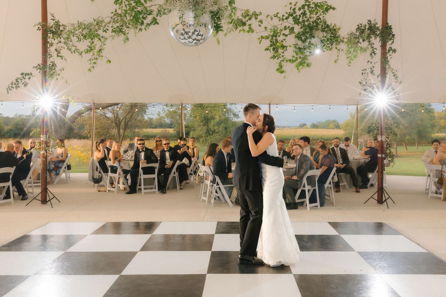 Bride and groom share their first dance on a classic black and white checkered dance floor at their reception.
