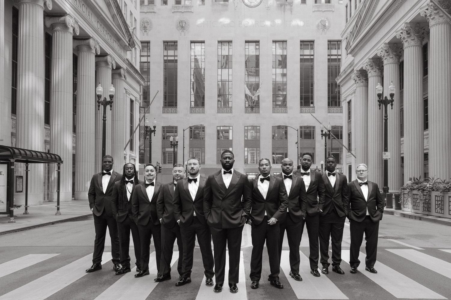 Black and white photo of a groom and groomsmen in tuxedos posing in an elegant columned building.