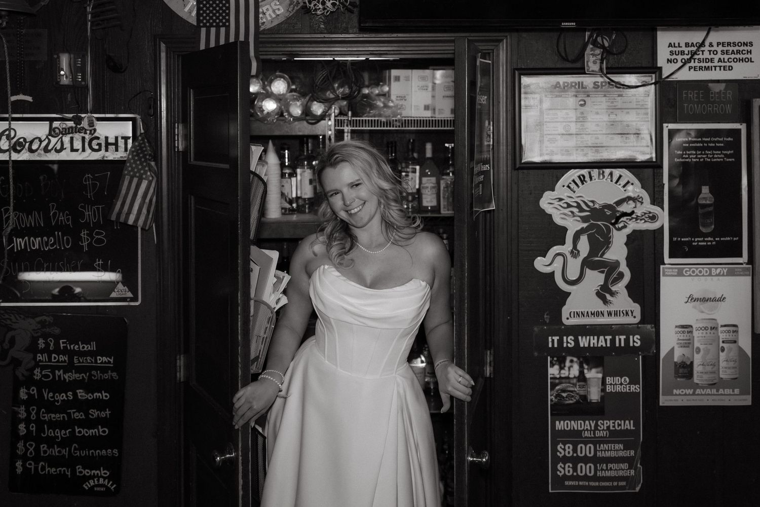 Bride in white strapless gown posing in a bar doorway, black and white wedding photo with Coors Light sign.