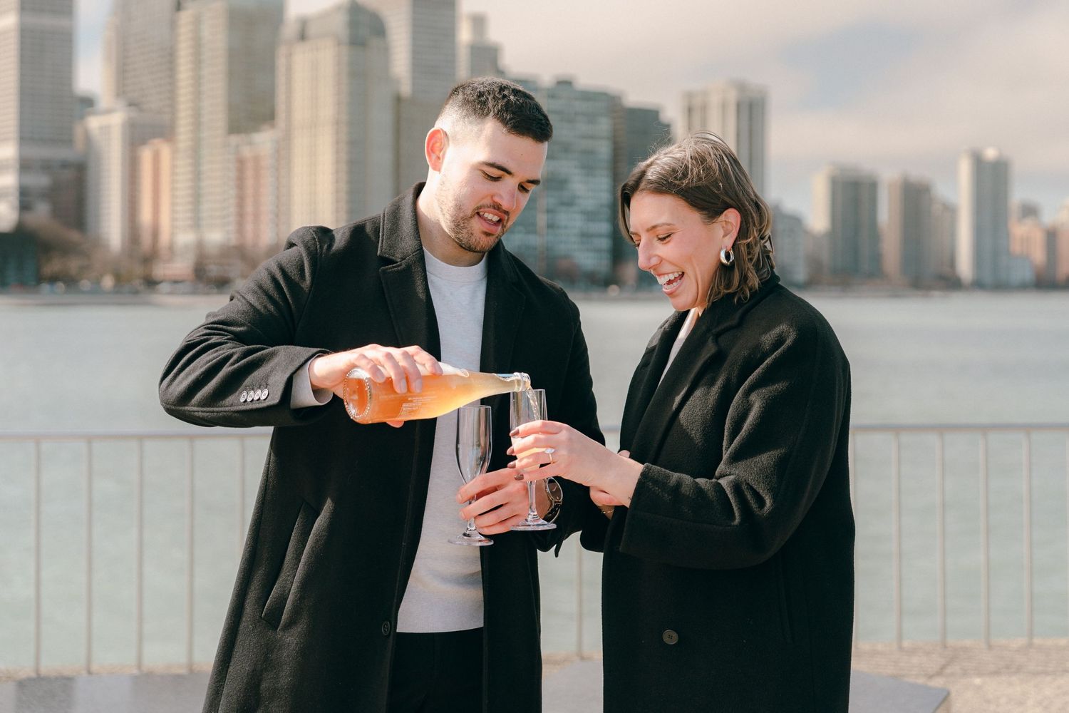 Couple pouring champagne together with a city skyline in the background.