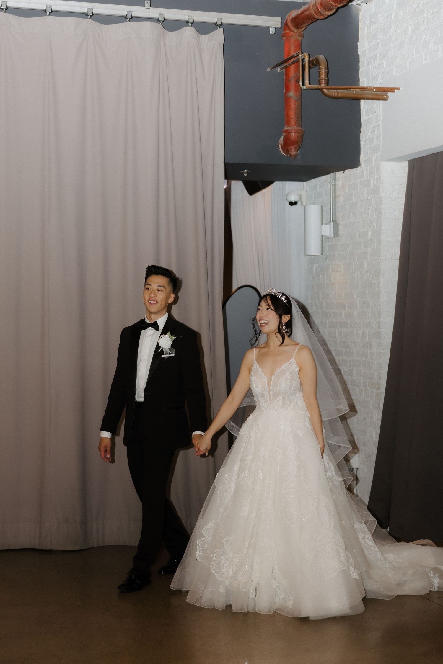 Bride in white ballgown and groom in black tuxedo holding hands at wedding venue.