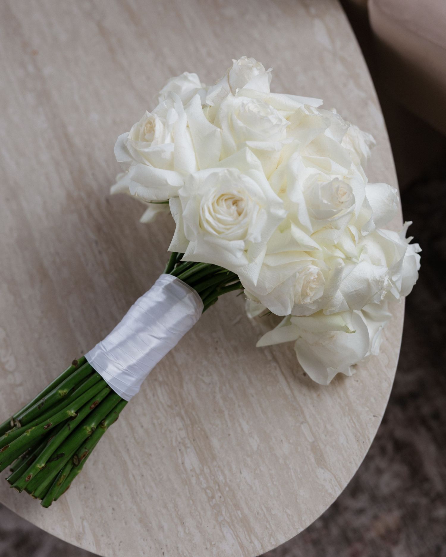 Elegant bridal bouquet of white roses wrapped in white ribbon, resting on a wooden table.