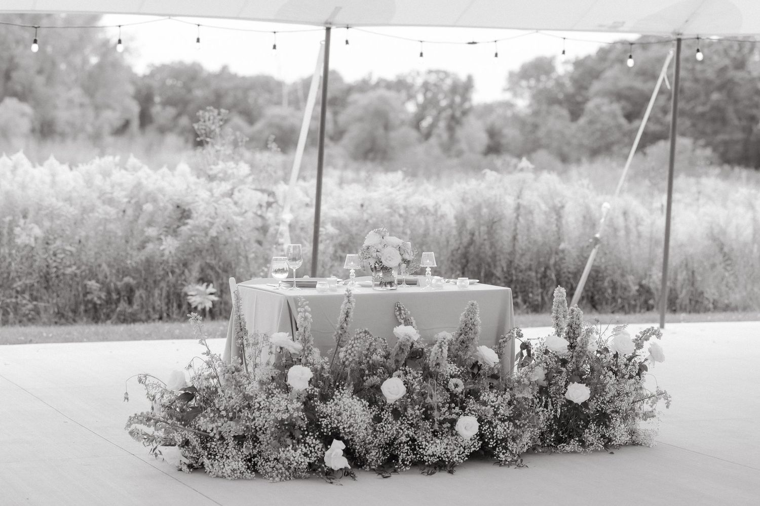 Black and white wedding sweetheart table adorned with lush floral arrangements under an elegant outdoor tent.