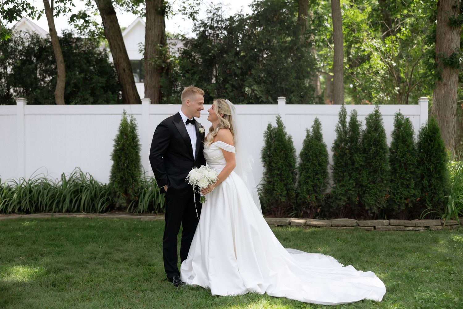 Bride and groom share a romantic kiss in a lush garden, bride wearing a white off-shoulder gown.