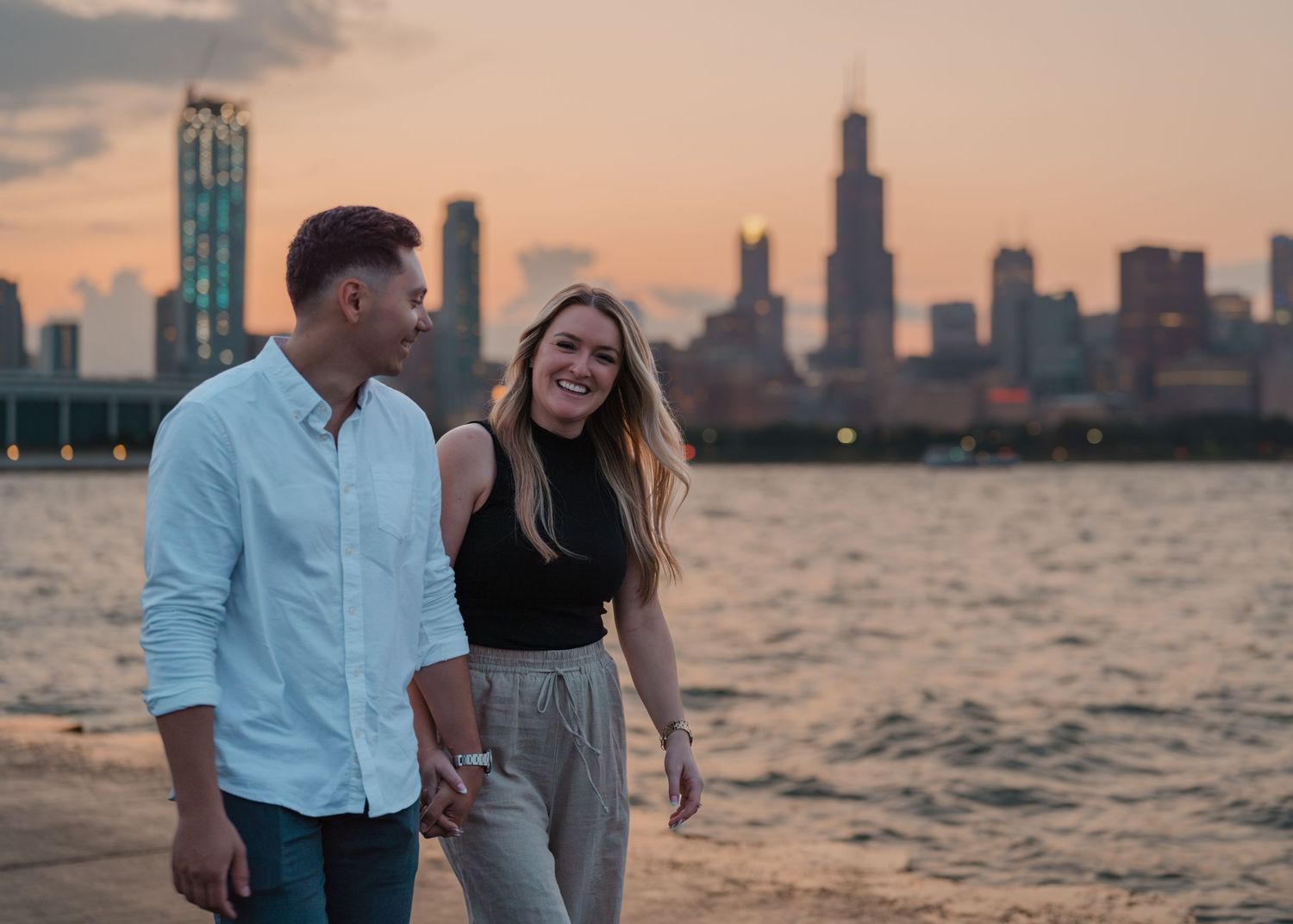Couple holding hands smiling at sunset with Chicago skyline and Willis Tower in the background.