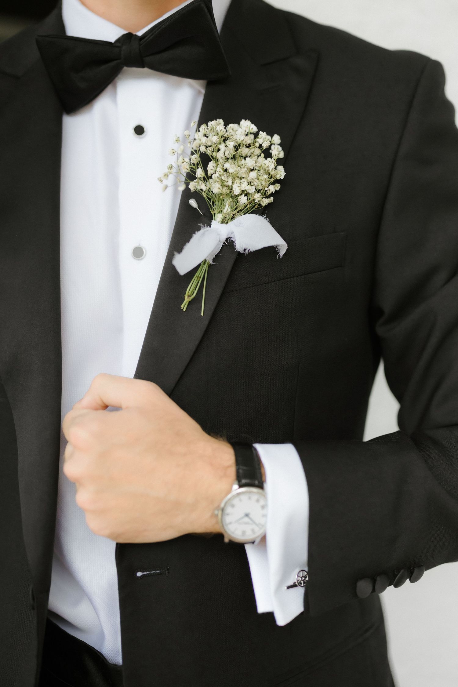 Close-up of groom's black tuxedo with baby's breath boutonniere and classic watch.