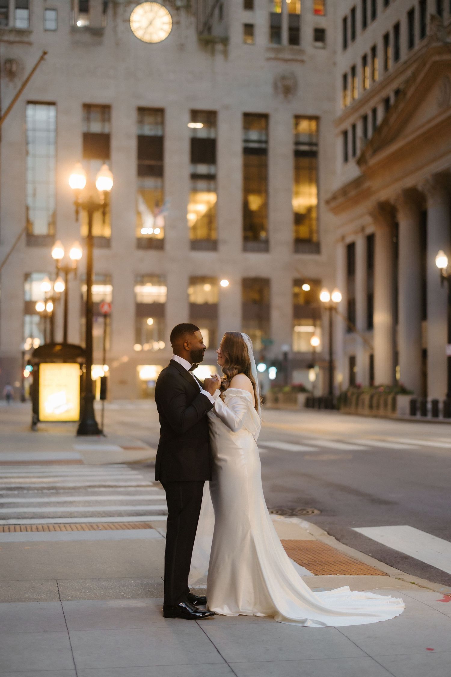 Bride and groom share a romantic moment on a city street at night, illuminated by warm glowing lights.