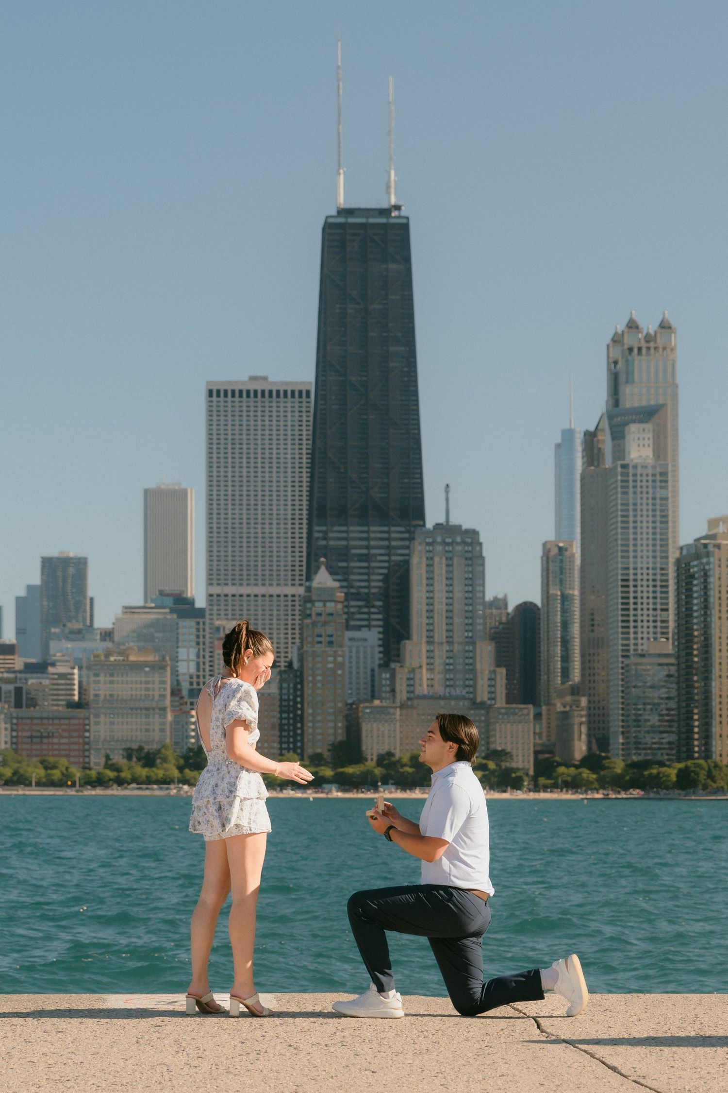 Man proposing on one knee to woman by Lake Michigan with Chicago skyline backdrop.