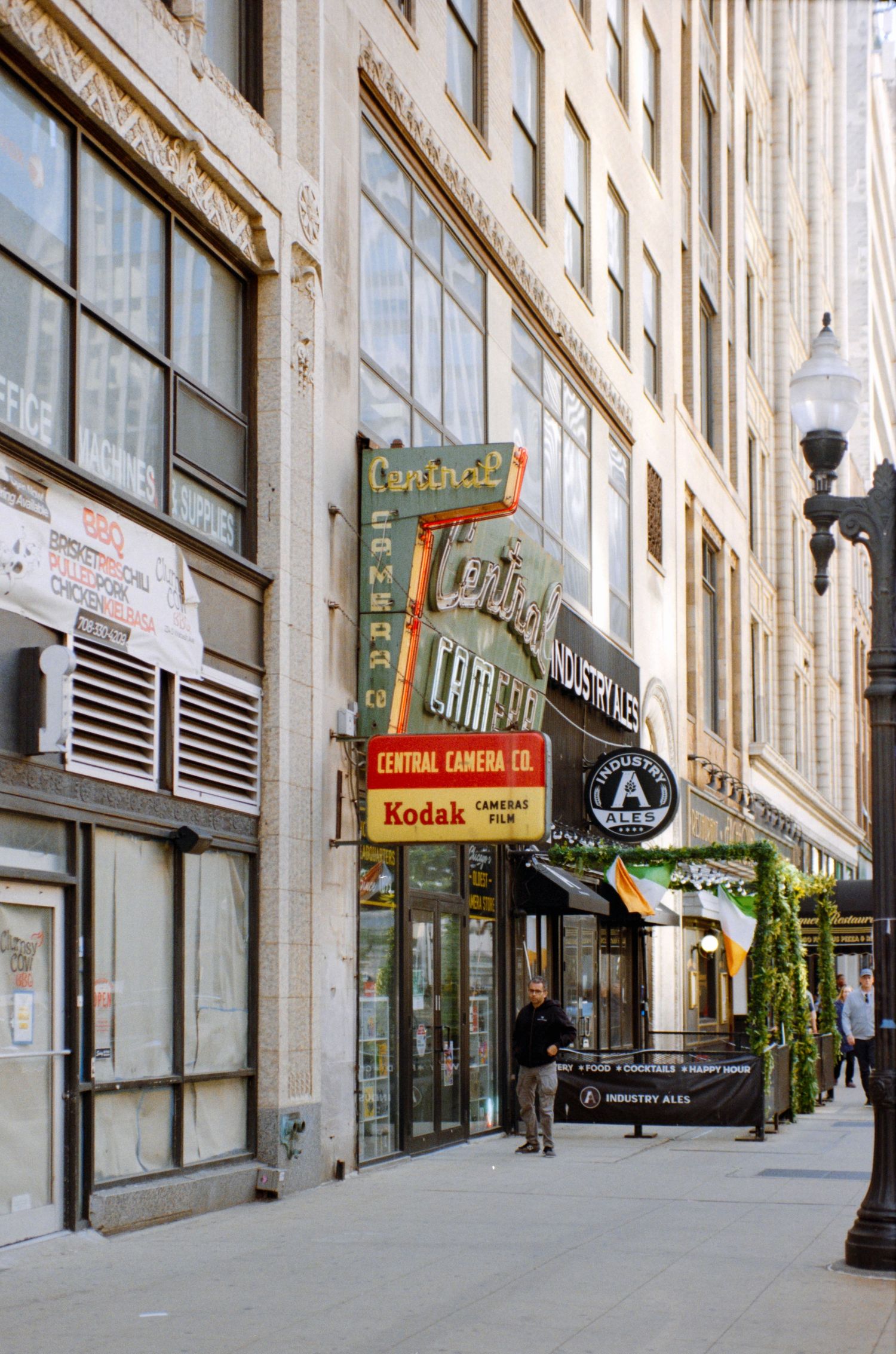 Central Camera Co. and Kodak store on a bustling city sidewalk flanked by tall historic buildings.