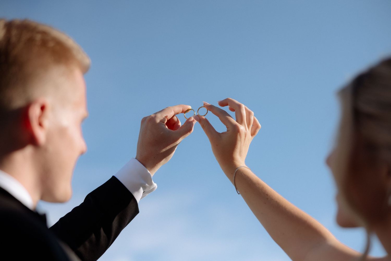 Bride and groom exchanging wedding rings against bright blue sky close-up detail shot.
