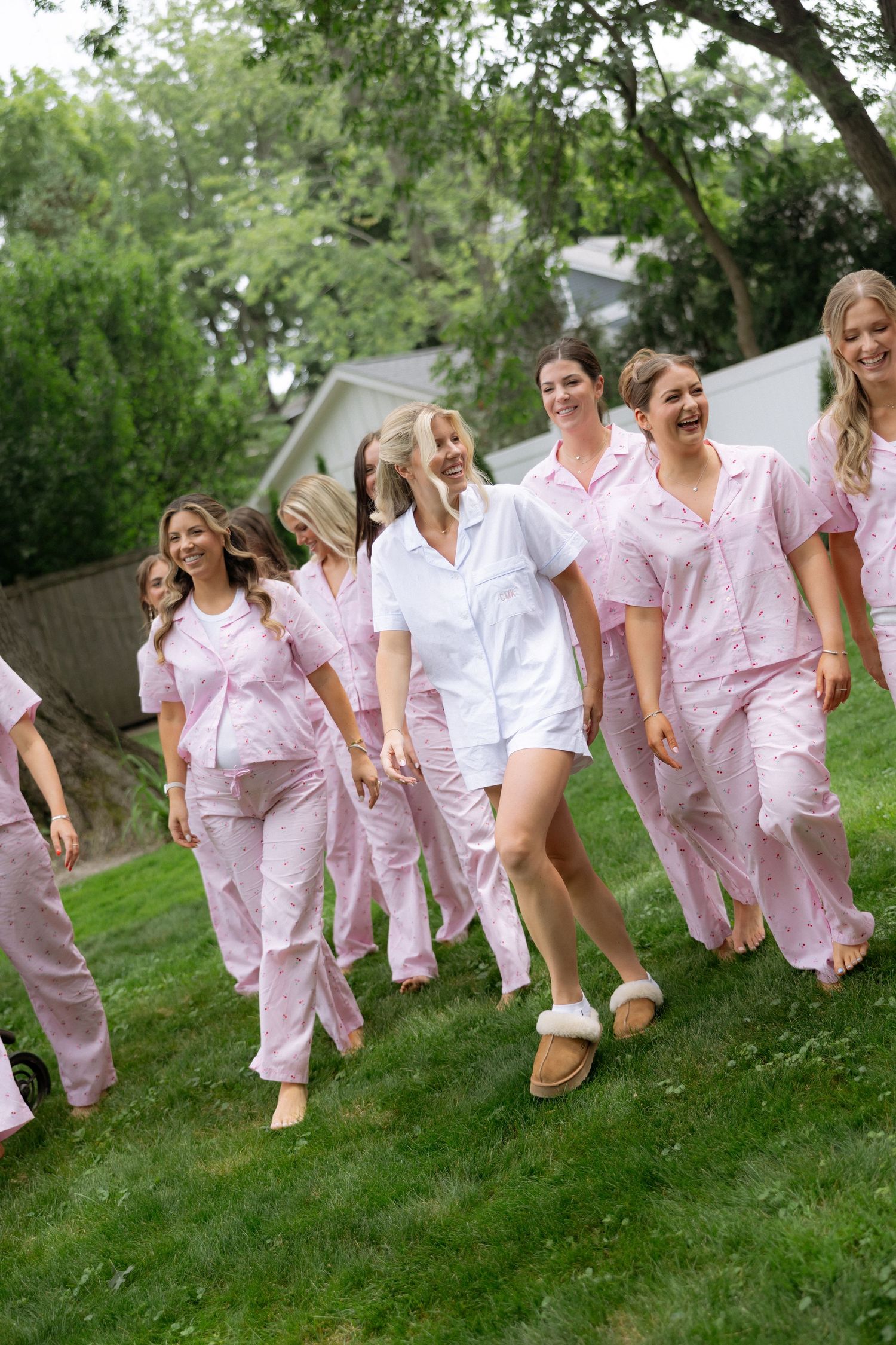 Bride and bridesmaids laughing outdoors in matching pink pajamas with bride in white set.