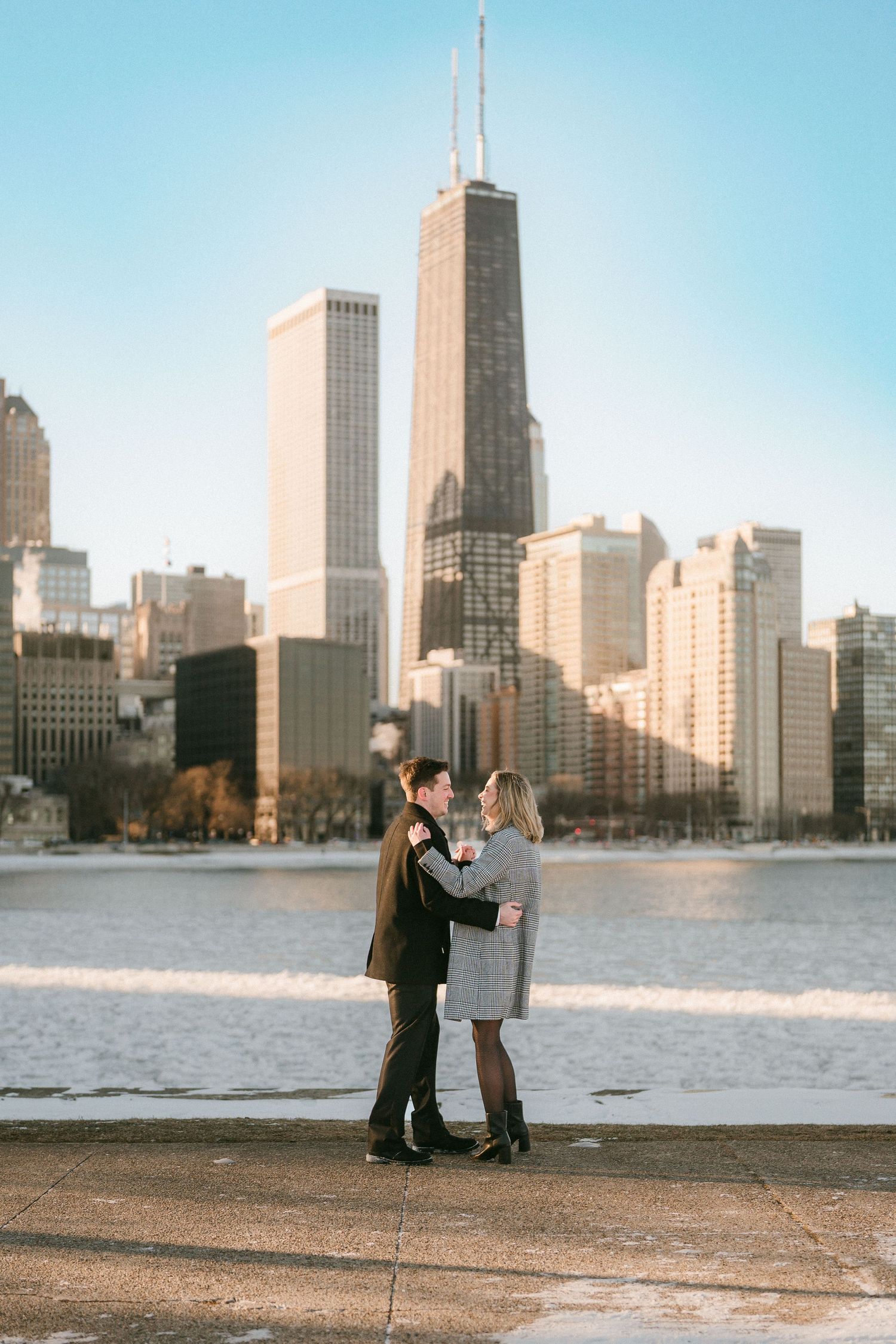 Couple embracing in front of Chicago skyline and frozen lake on a clear winter day.