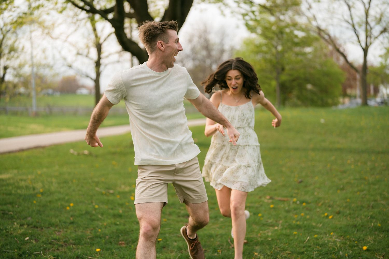 A joyful couple runs hand-in-hand through a lush green park on a spring day.