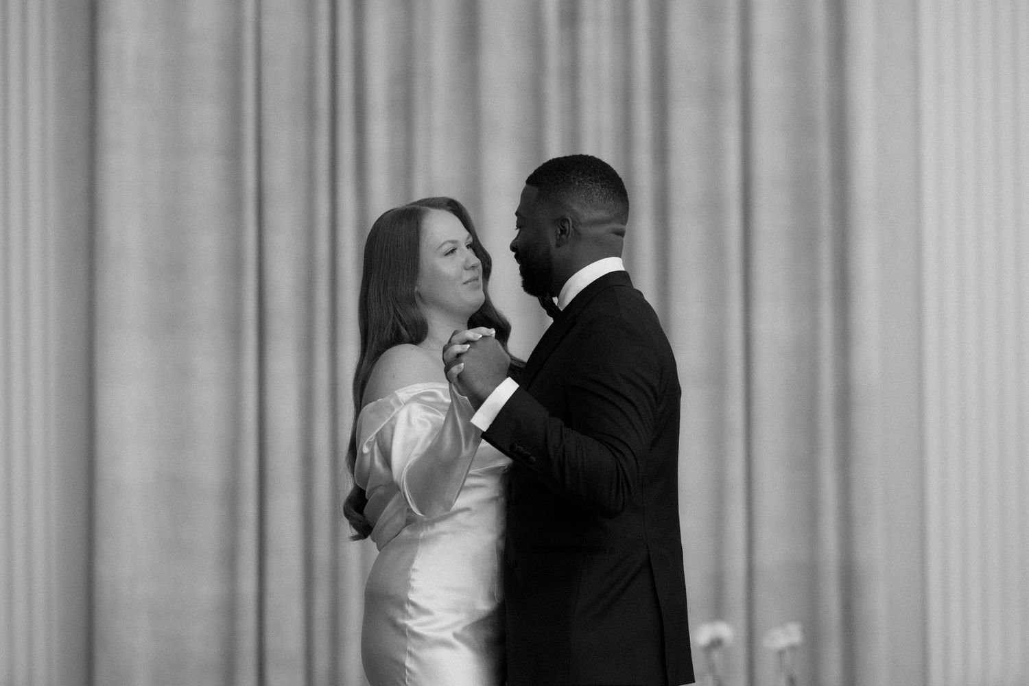 Black and white photo of an interracial couple sharing their first dance at an elegant wedding reception.