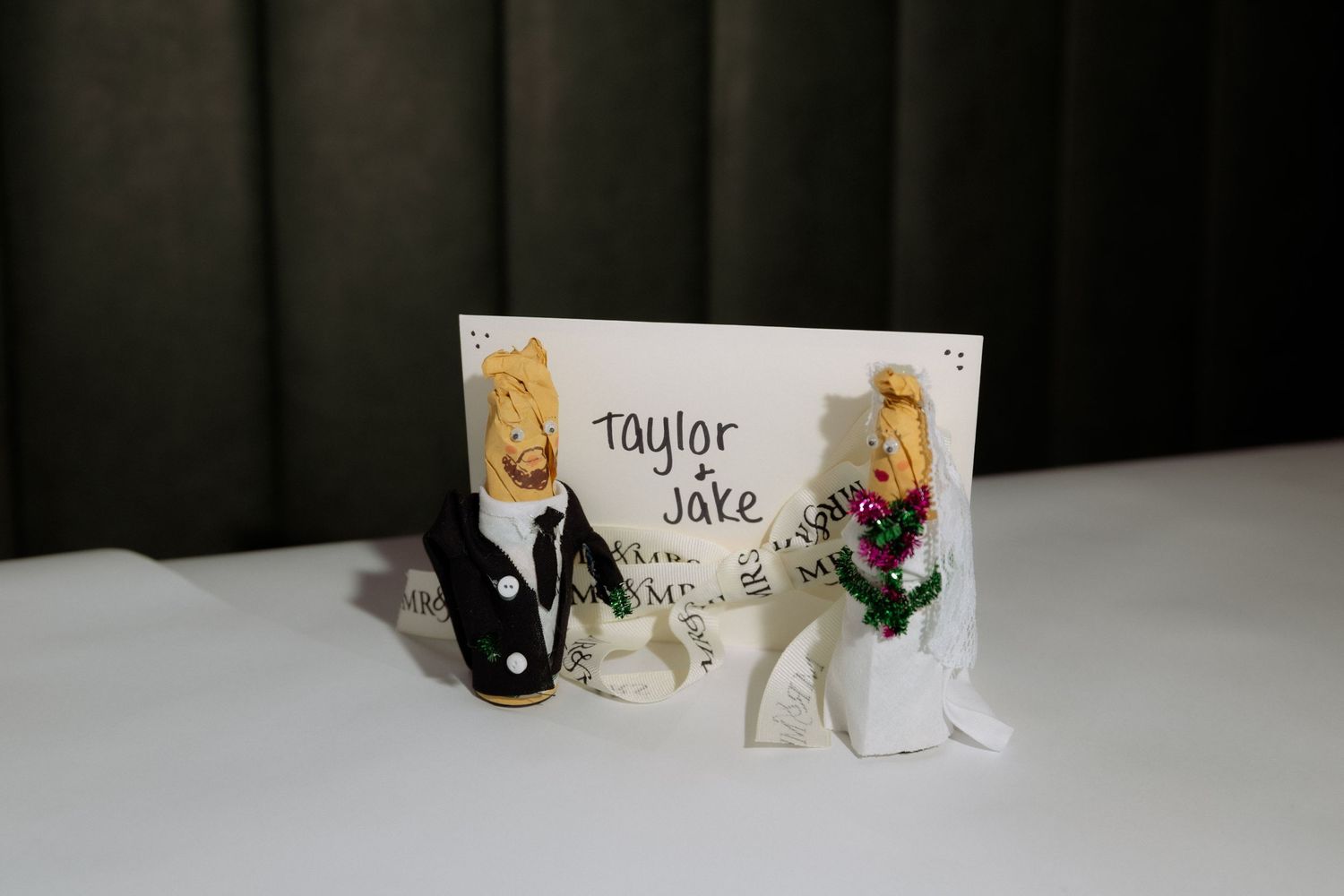 Taylor and Jake wedding cake toppers dressed as bride and groom on a white table.