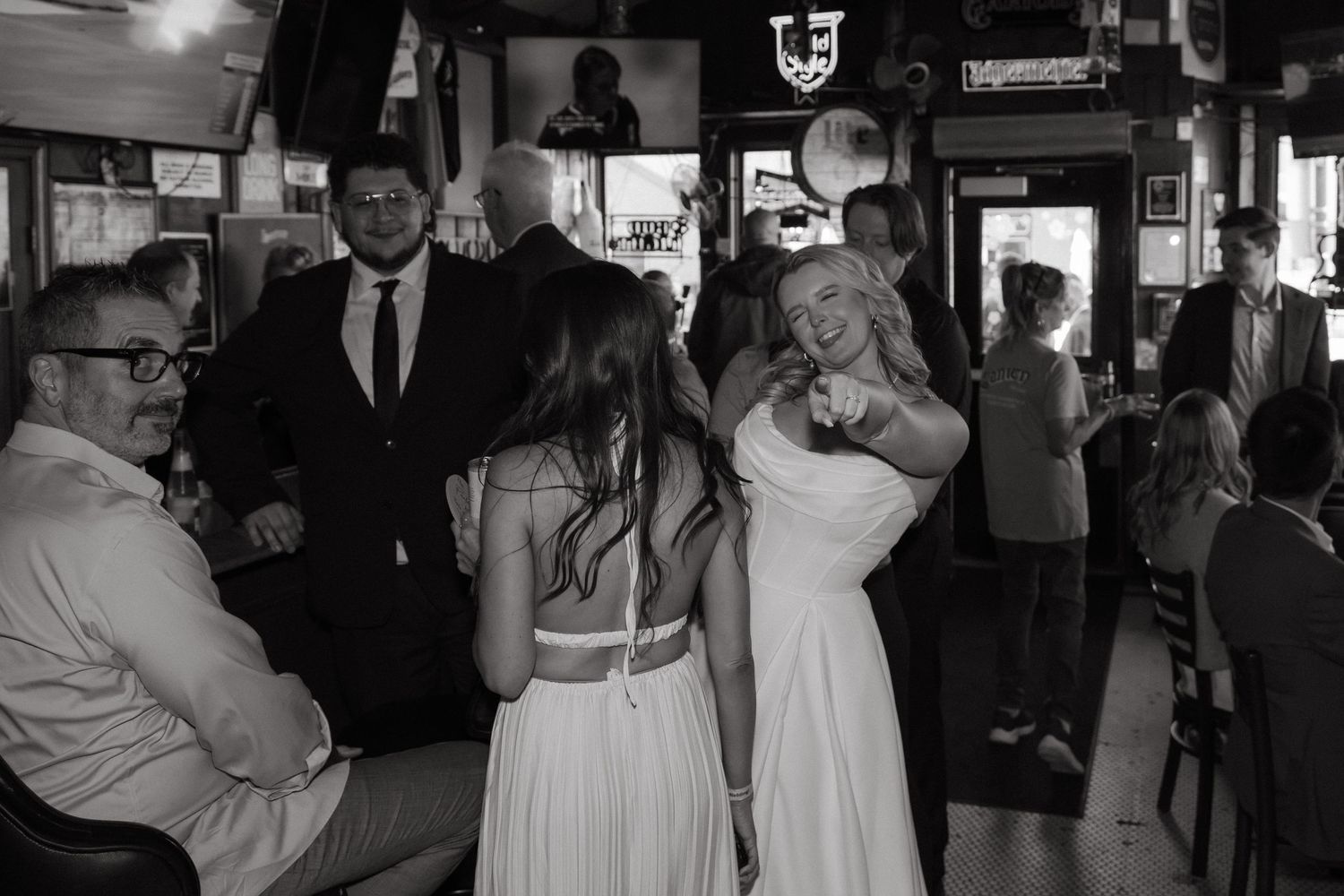 Black and white photo of a bride dancing with a guest at a wedding reception inside a bar venue.