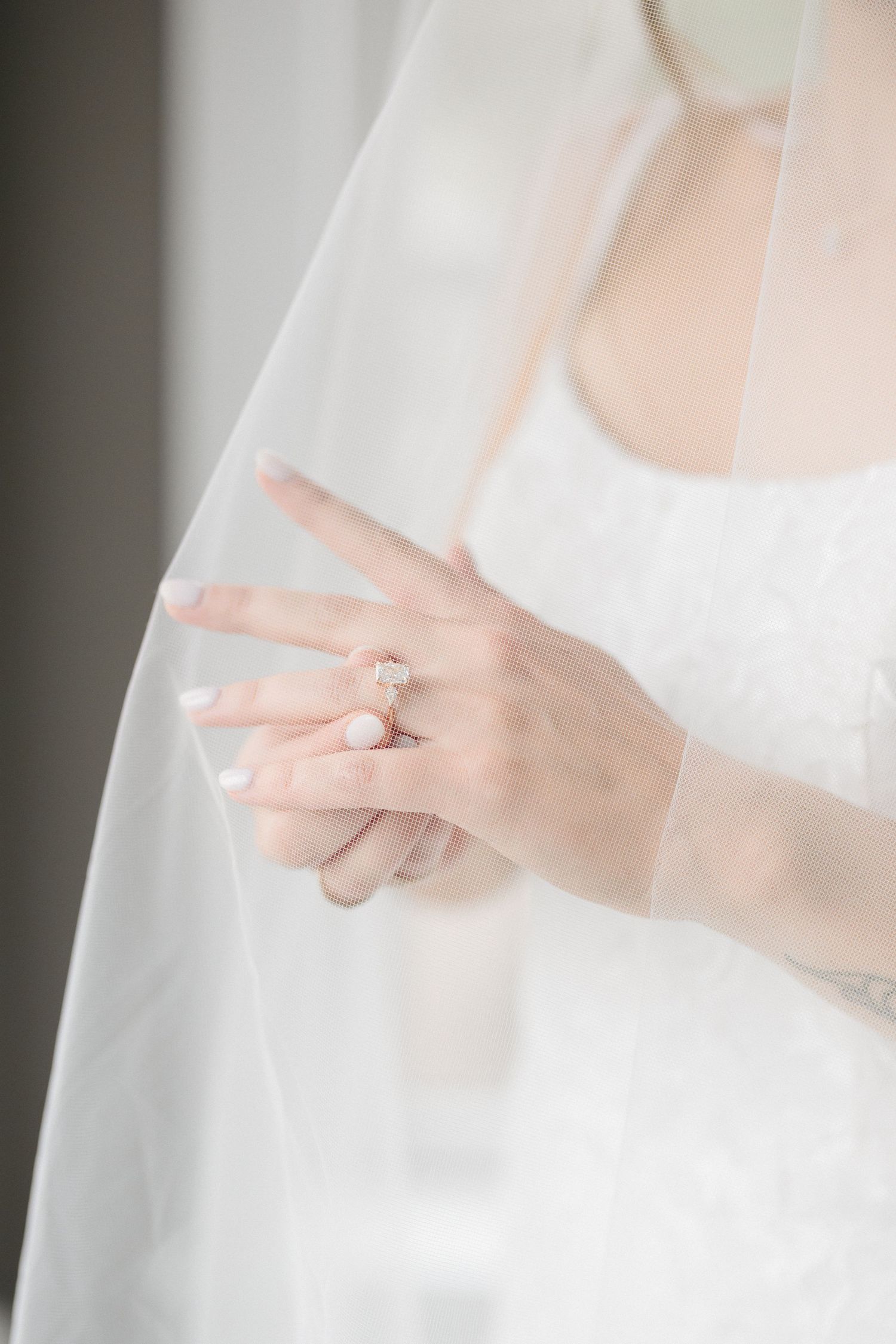 Close-up of bride's hand wearing a diamond engagement ring with wedding veil draped over.