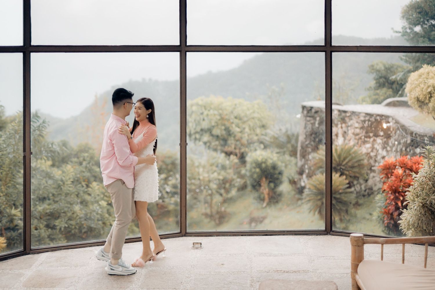Couple embracing near large windows with lush green mountain views in a bright modern space.