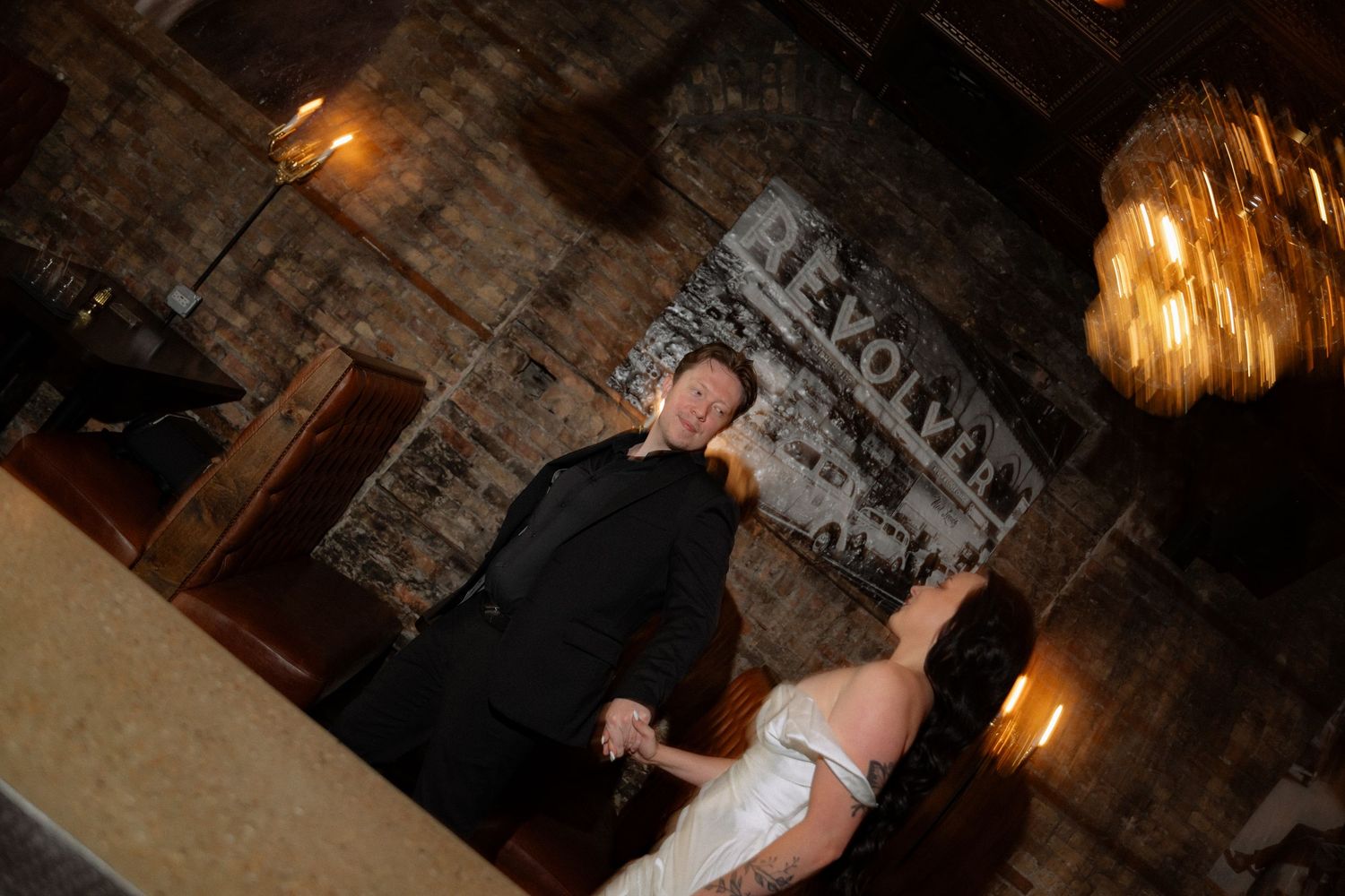 Couple sharing first dance in rustic brick venue with warm chandelier lighting during wedding reception.