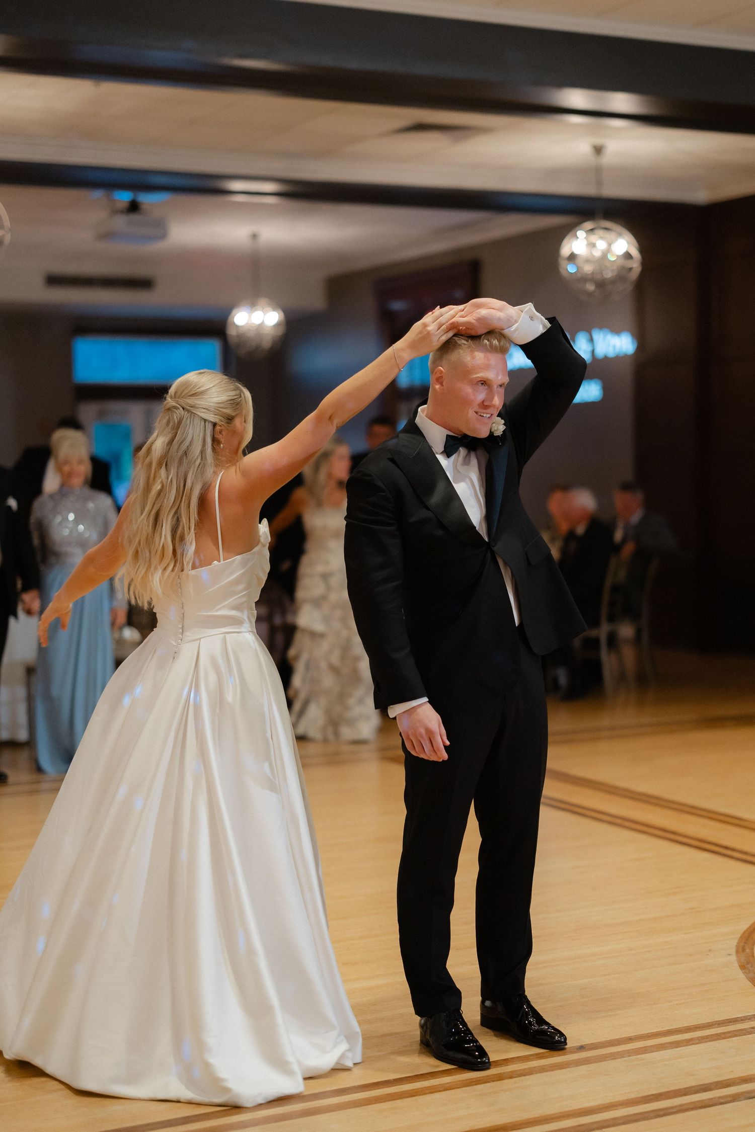 Bride and groom sharing first dance as bride spins groom under her arm at wedding reception.