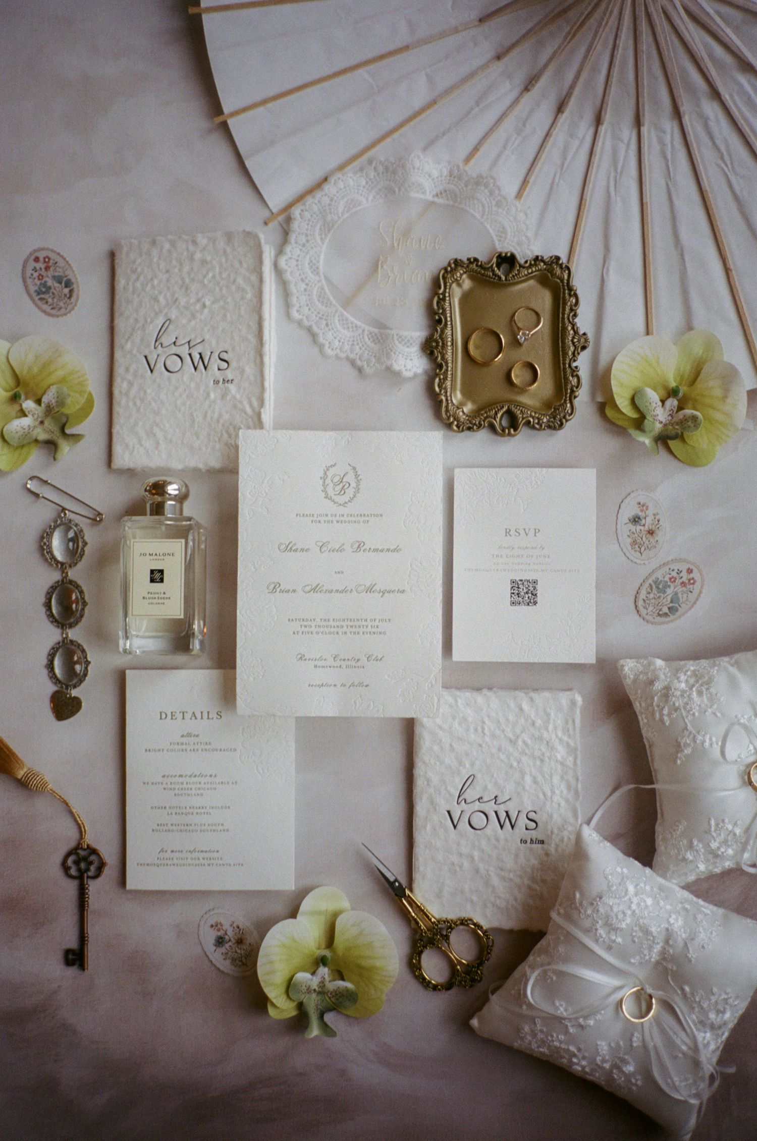Elegant wedding stationery flatlay with vow books, invitation suite, gold ring dish, floral accents, and Jo Malone perfume.