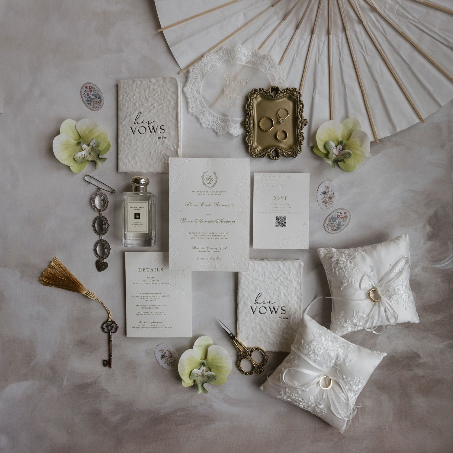 Elegant wedding flat lay with vow books, invitation suite, Jo Malone perfume, ring pillow, and floral accents on marble.