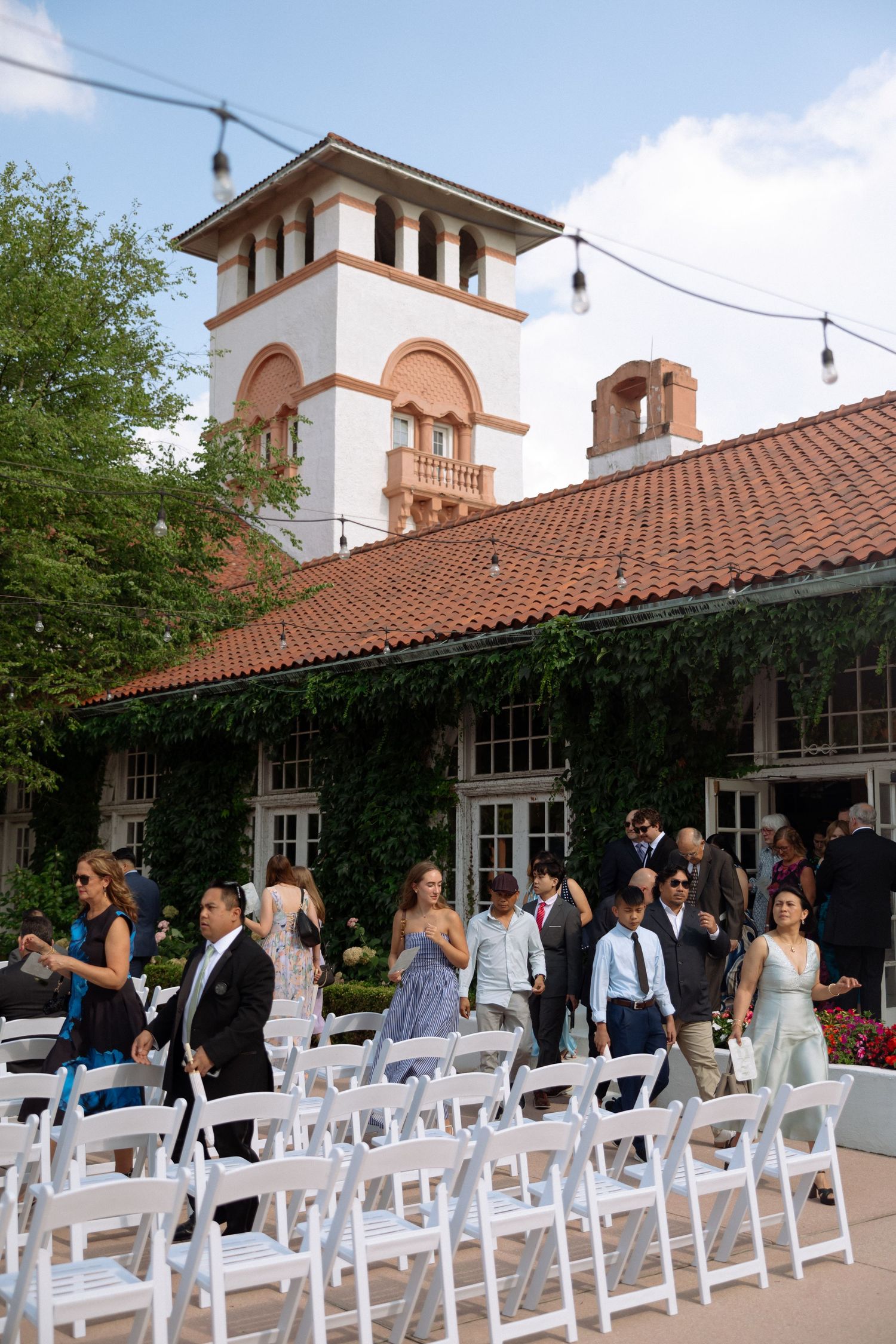 Wedding guests arriving at an elegant outdoor ceremony venue with Spanish architecture and red tile roof.
