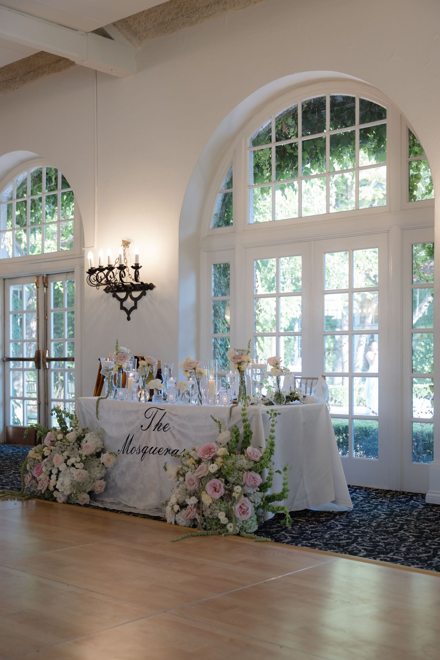 Elegant wedding sweetheart table adorned with pink and white floral arrangements beneath arched windows.