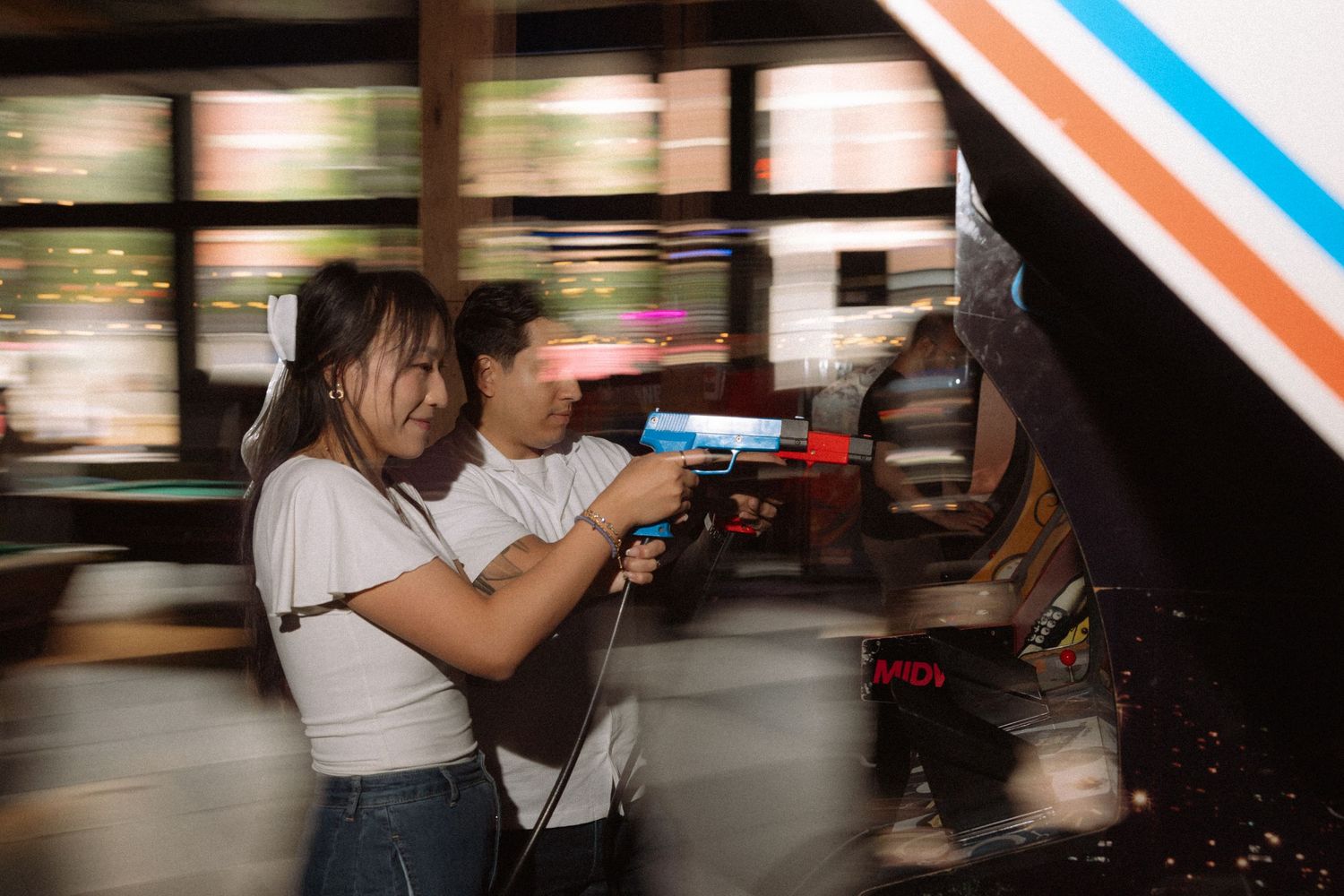 Young woman aiming light gun at arcade shooting game with motion blur effect in background.