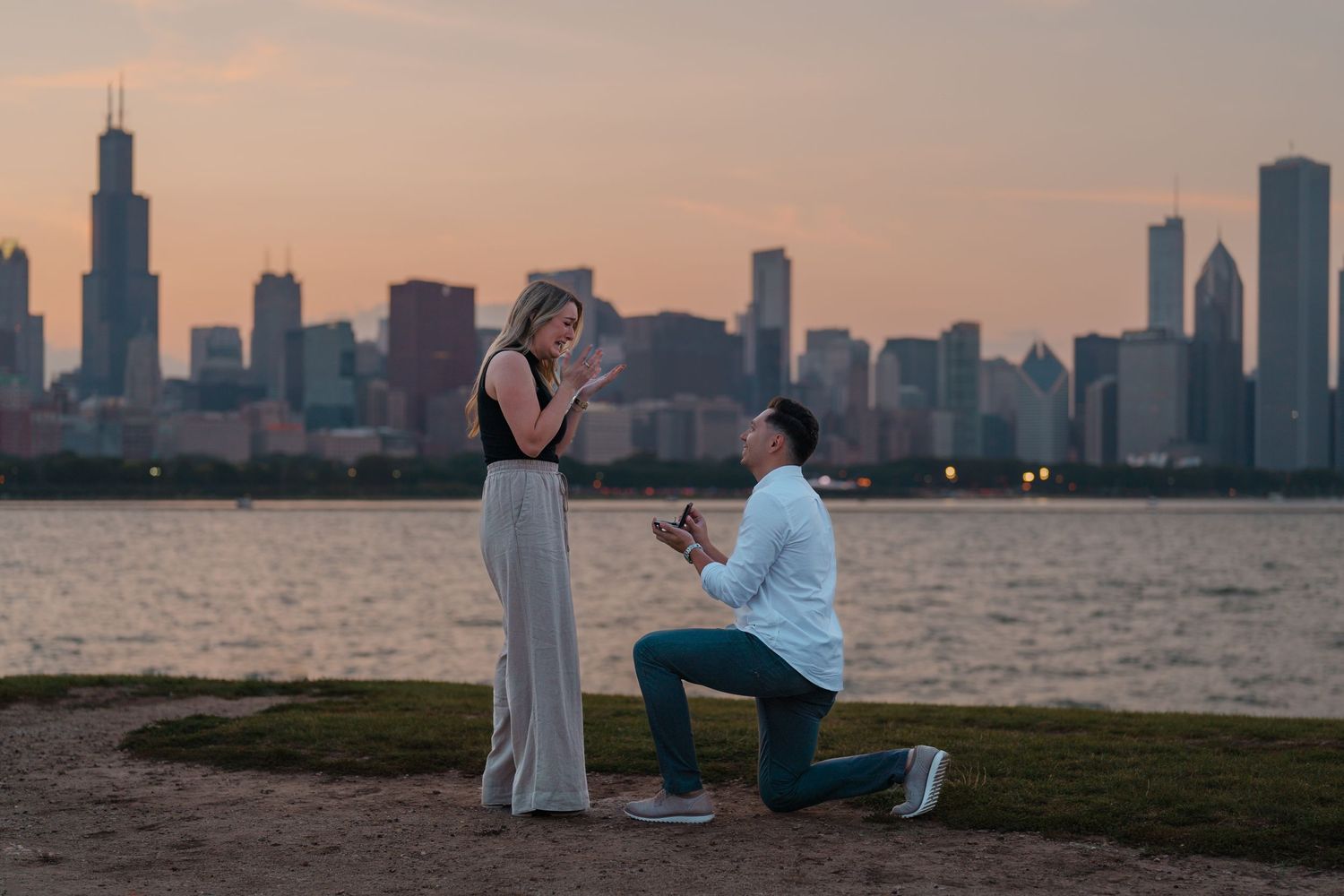 Man proposing on bended knee to surprised woman with Chicago skyline at golden hour.