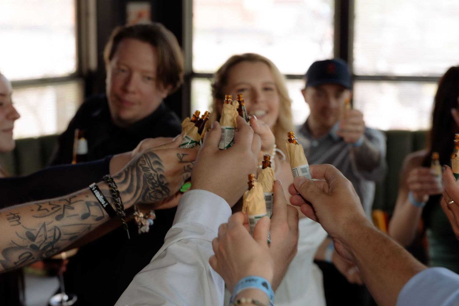Group of friends raising beer bottles in a celebratory toast at a casual indoor gathering.