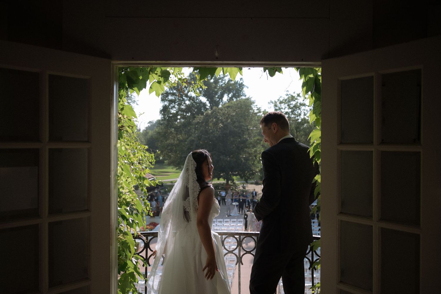 Bride and groom silhouetted in doorway overlooking lush garden at elegant outdoor wedding venue.