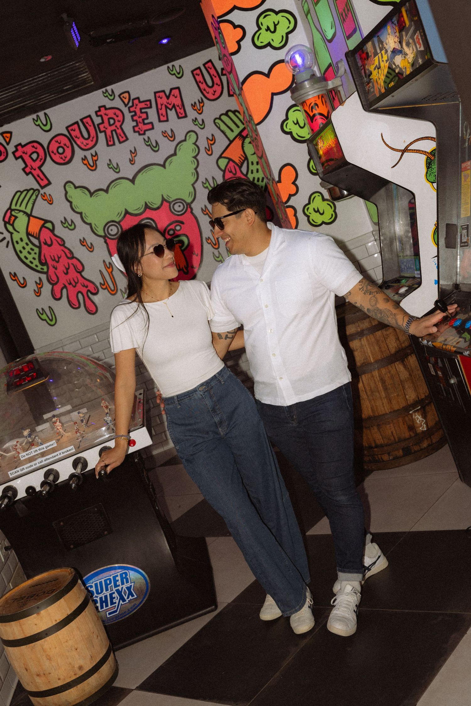 Smiling couple posing together in front of colorful arcade game mural artwork.