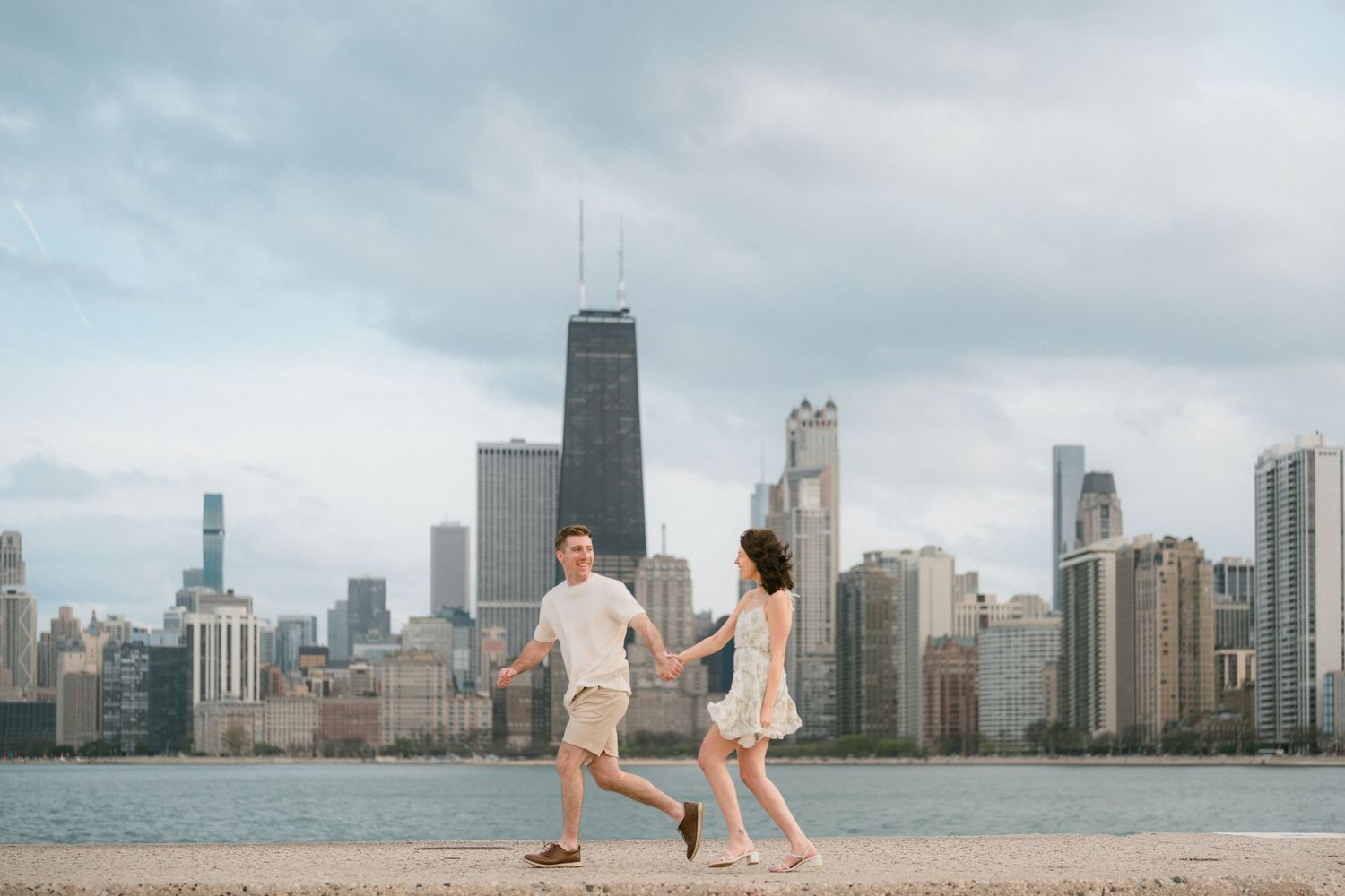 Couple holding hands and running along Chicago lakefront with city skyline.