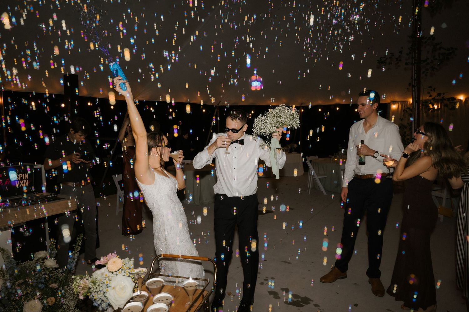 Bride and groom celebrate with confetti cannons and bubbles at their outdoor wedding reception at night.
