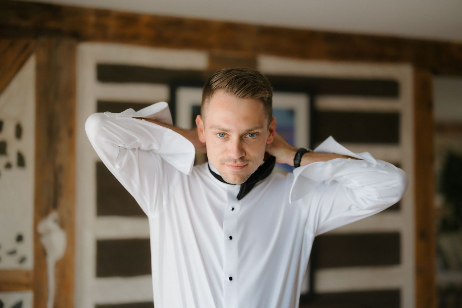 Groom in white dress shirt adjusting collar while getting ready for wedding ceremony.