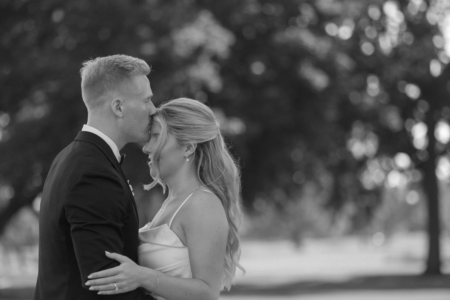 Black and white photo of bride and groom sharing intimate moment outdoors with bokeh background.