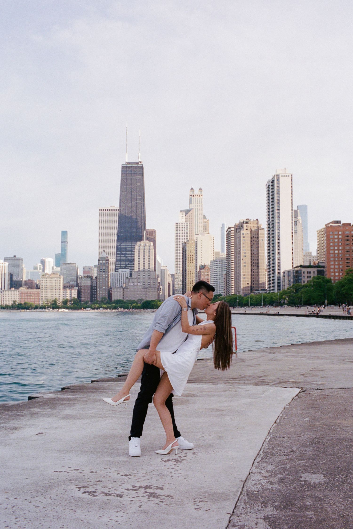 Couple sharing a romantic dip kiss on Chicago lakefront with iconic city skyline backdrop.